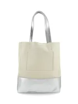 Cartera tipo tote de cuero color crudo con base y asas plateadas, de diseño vertical y rectangular con detalle de placa metálica con logo de la marca en el frente.
