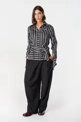 Camisa de manga larga con diseño de rayas verticales y horizontales, confeccionada en poliéster. Presenta cuello clásico, cierre frontal de botones y cintas integradas en la cintura para anudar y ajustar la prenda. Incluye aberturas en los puños.