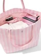 Bolso tote de mano tipo shopper, de tela de nailon con diseño a rayas rosadas y blancas. Cuenta con cierre superior de cremallera, asas de piel sintética y herrajes dorados.