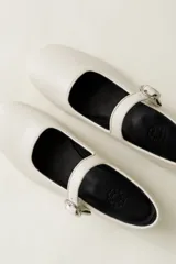 Zapato plano estilo Mary Jane de cuero negro, con punta fina y tira ajustable con hebilla sobre el empeine.