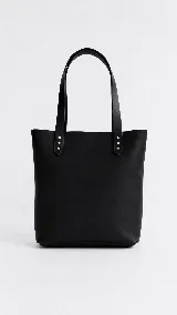 Cartera tipo tote bag de cuero marrón, con diseño minimalista, asas largas y detalles de remaches metálicos en la unión de las asas.