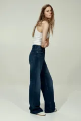 Jean de tiro alto con corte wide leg, confeccionado en denim de algodón rígido. Presenta diseño clásico de cinco bolsillos, cierre frontal con botón y acabado de lavado azul medio con efecto desgastado.