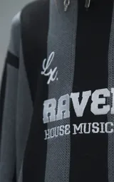 Sweater de punto con diseño a rayas verticales en negro y gris, cuello redondo y mangas largas. Presenta un estampado gráfico frontal con estilo deportivo retro que incluye el texto 'Ravers' y el número '90'. Cuenta con terminaciones en punto rib en cuello, puños y ruedo.