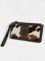 Billetera porta celular confeccionada en cuero marrón con detalle de pelo vacuno con estampado animal print tipo vaca en tonos blancos, marrones y negros. Cuenta con correa de muñeca y cierre superior.