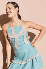 Top corto color turquesa con tirantes finos y detalles de volantes brillantes en color beige que forman un patrón geométrico en el frente.