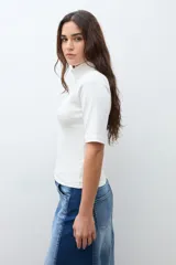 Remera de cuello alto tipo media polera, de manga corta y corte ajustado al cuerpo, en color crudo.