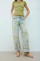 Jeans de tiro bajo y corte holgado, color celeste con estampado floral en tonos amarillos y verdes. Presenta diseño de cinco bolsillos, trabillas para cinturón y dobladillo con vuelta en los bajos. Cierre frontal con cremallera y botón metálico.