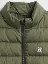 Chaleco puffer acolchado de color beige, con cierre frontal de cremallera, cuello alto y logo de la marca bordado en el pecho.