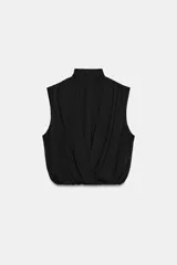 Blusa sin mangas blanca con estampado de lunares negros, cuello alto drapeado y nudo frontal en el bajo.