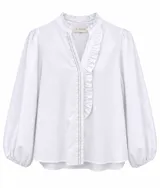 Camisa blanca de manga larga abullonada, con escote en V y cuello mao con volados. Presenta un volado decorativo en el frente y costuras en contraste.
