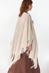 Ruana de punto color beige con diseño abierto y flecos en los bordes.