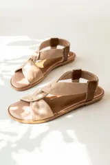 Sandalias chatitas de cuero en tono nude, con diseño de tiras cruzadas en el empeine y elástico en el talón para mayor ajuste. Presentan una plantilla acolchada y detalles en cuero charolado en la parte posterior.
