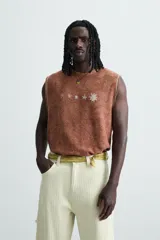Camiseta tank (sin mangas) de corte relajado, color terracota con efecto lavado y estampado frontal de estrellas en blanco. Presenta cuello redondo y acabados deshilachados en las sisas y el ruedo.