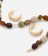 Conjunto de bijouterie compuesto por un collar corto de cuentas irregulares de resina en tonos tierra, verde y beige, y aros de argolla gruesa dorada.