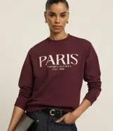 Saco de algodón color bordó con cuello redondo y mangas largas. Tiene ribete en cuello, puños y bajo. Estampado frontal con la leyenda "Paris - Champs Élysées - Est. 1965".