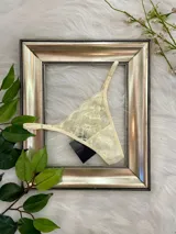 Microtanga de encaje color champagne con diseño floral, laterales regulables y forro interno de algodón.