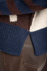 Sweater de punto con diseño combinado, presentando un estampado de manchas de vaca en el cuerpo y mangas con rayas horizontales en tonos azul y marrón. Posee cuello redondo y puños acanalados.