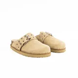 Zueco de gamuza color natural con suela de corcho y goma. Presenta una correa ancha con hebilla metálica y ojales decorativos en el empeine.