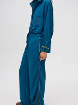 Camisa azul de corte holgado, con cuello camisero, mangas largas con detalles en los puños, bolsillo frontal con bordado y cierre delantero con botones.