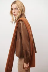 Chaqueta color camel con cuello camisero, cierre frontal con botones dorados, dos bolsillos de parche en el pecho y costuras decorativas en contraste.