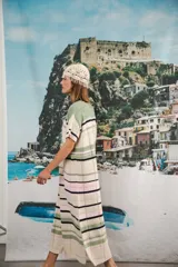 Vestido largo de tejido calado con rayas horizontales en tonos beige, marrón y amarillo. Tiene corte recto, hombros caídos, tajo lateral y logo bordado en la manga.