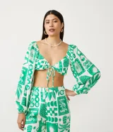 Blusa cropped blanca con estampado de motivos verdes, escote corazón con lazo, mangas largas abullonadas y confeccionada en tricolina.