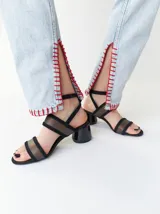 Sandalias de tacón redondo de 6 cm, con diseño de tiras en gamuza negra y bandas frontales translúcidas de TPU. Incluye cierre con pulsera fina al tobillo.