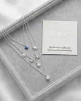Collar triple de plata 925 con dijes colgantes que incluyen un ojo turco, caracoles de mar, estrellas de mar y una circonia central.