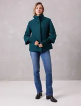 Tapado de tejido bouclé color marrón, con silueta evasé y largo a la cadera. Presenta cuello alto envolvente, cierre frontal oculto con botones a presión y bolsillos frontales de gran tamaño. Sus mangas son 3/4 con corte amplio y puños de tejido rib al tono que se extienden para cubrir las muñecas.