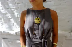 Collar artesanal con dije central de metal con textura orgánica irregular que evoca una ostra. El dije está montado sobre un cordón de algodón natural, permitiendo un uso versátil y regulable.