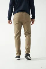 Pantalón chino color beige, de corte slim, con bolsillos laterales y traseros. Se ajusta a la cintura con cinturón de cuero marrón.