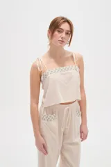 Musculosa de viscosa color natural, con breteles finos ajustables con lazos, cuello cuadrado y detalle bordado geométrico en el escote.