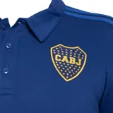 Chomba azul con cuello clásico y tapeta de botones. Presenta las tres tiras características de Adidas en los hombros y el logo de la marca bordado en dorado en el pecho. También incluye el escudo del club Boca Juniors bordado en el pecho.