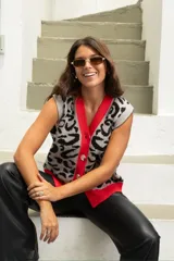 Chaleco de punto con diseño animal print en tonos gris y negro, con cuello en V y borde frontal en color rojo vibrante. Presenta cierre frontal con botones grandes y corte holgado.