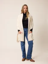 Poncho abierto de tejido de punto en color gris claro con bordes y detalles de bolsillos en gris oscuro. Presenta un diseño holgado y versátil con placa metálica decorativa en uno de los bolsillos frontales.