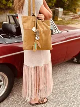 Bolso tipo tote de gamuza color camel, con doble asa de mano y correa larga extraíble y ajustable. Tiene dos bolsillos externos grandes y cierre superior.