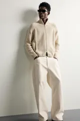 Chaqueta relaxed fit de punto tejido en hilatura con mezcla de algodón, color beige, con cuello subido y manga larga. Cuenta con acabados en rib, efecto lavado y cierre frontal con cremallera.