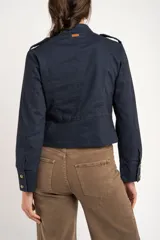 Chaqueta corta color beige de algodón, de inspiración militar con cuello mao y doble botonadura frontal con botones metálicos dorados.