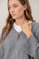Campera de punto gris con cierre frontal completo, cuello redondo y mangas anchas. Presenta un detalle de tirador de cuero en el cierre.