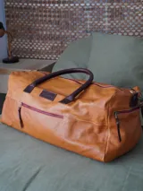 Bolso weekender de cuero color miel, con asas y detalles en marrón oscuro, bolsillos externos con cierres metálicos y forro interior.
