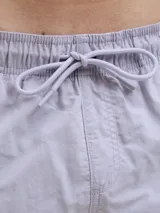 Short de baño de tiro medio en color lila, con cintura elástica y cordón ajustable. Presenta un diseño minimalista con el logo de la marca estampado en la parte inferior derecha.