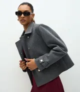 Saco corto de corte regular confeccionado en polivelour gris, con cuello inglés, cierre frontal de doble abotonadura con botones dorados y mangas largas con detalle de trabas en los puños.