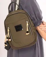 Mochila de nylon color verde oliva, con compartimento principal y bolsillo frontal con cierre metálico. Presenta detalles de cordones decorativos en los tiradores de los cierres, una grifa de goma con el logo de la marca y correas ajustables.