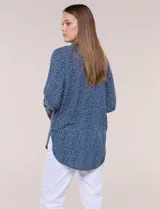 Camisa de rayón azul marino con estampado de lunares pequeños en tonos claros, cuello camisero, cierre frontal de botones, mangas largas y ruedo curvo asimétrico más largo en la espalda.