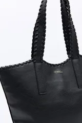 Cartera tipo tote de diseño amplio y textura símil cuero, con asas trenzadas y terminaciones artesanales.