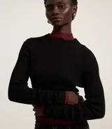 Blusa de punto acanalado en color beige, con cuello alto y mangas largas. Presenta un diseño ajustado al cuerpo con un detalle de borde en color marrón en el cuello y en el ruedo.