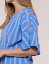Blusa de corte cuadrado y silueta amplia, color azul con diseño de rayas verticales en tonos más claros. Cuenta con cuello redondo y mangas cortas acampanadas, decoradas con una hilera de botones de madera sobre los hombros.
