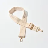 Correa de tela color beige con diseño geométrico en relieve y herrajes metálicos dorados.