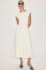 Vestido midi de crepe color blanco marfil, sin mangas, con cuello redondo y corte en la cintura. Falda con vuelo evasé y cierre lateral con cremallera oculta.