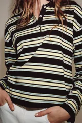 Polo de manga larga confeccionado en algodón, con diseño a rayas horizontales en tonos amarillos, verdes y oscuros. Presenta cuello solapa, cierre frontal con botones y bajo recto.